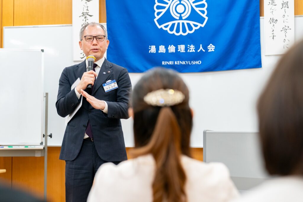 湯島倫理法人会の横断幕の前で自らの経験を講話する経営者