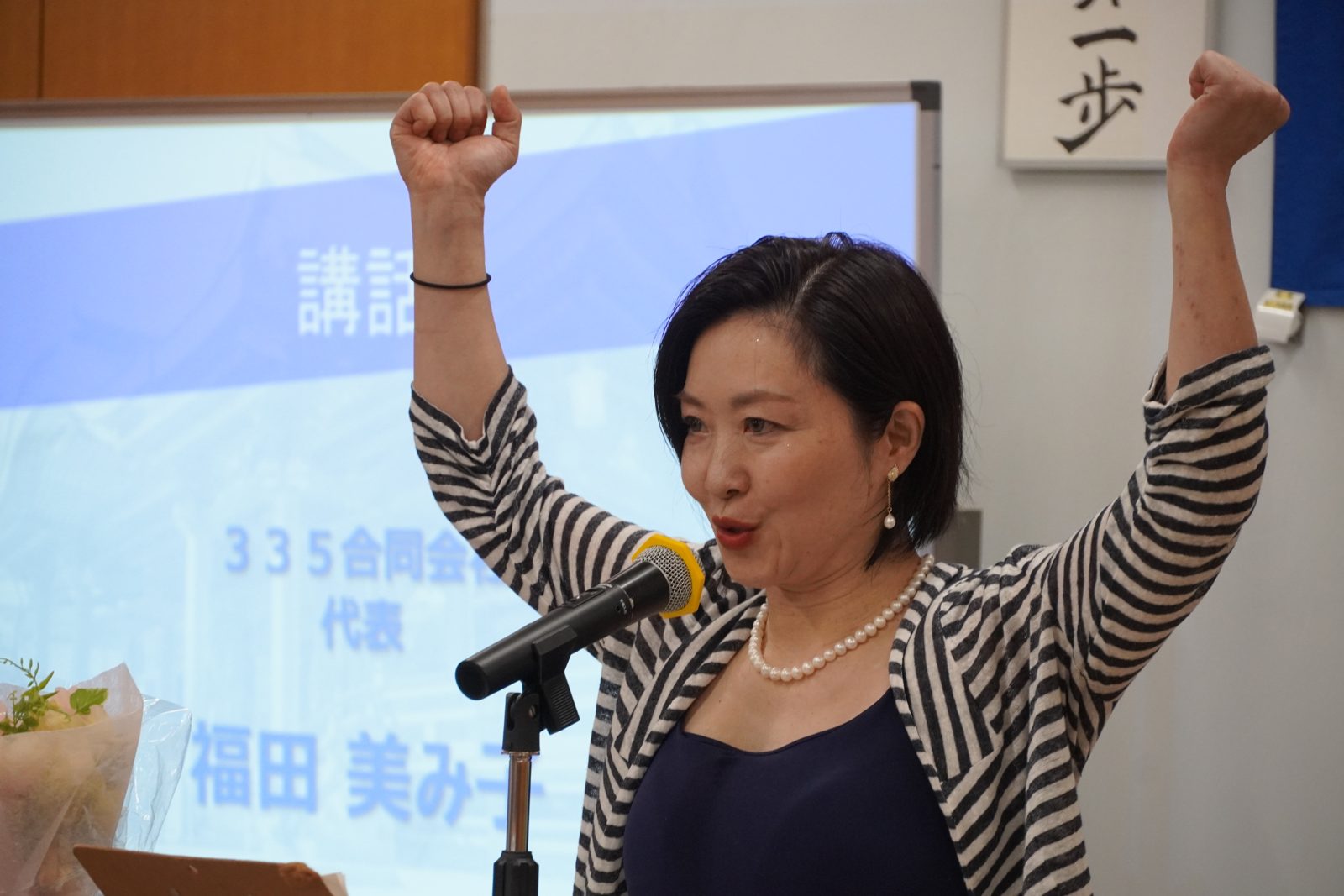 両腕を突き上げ、想定外を面白がる生き方を語る福田美み子氏