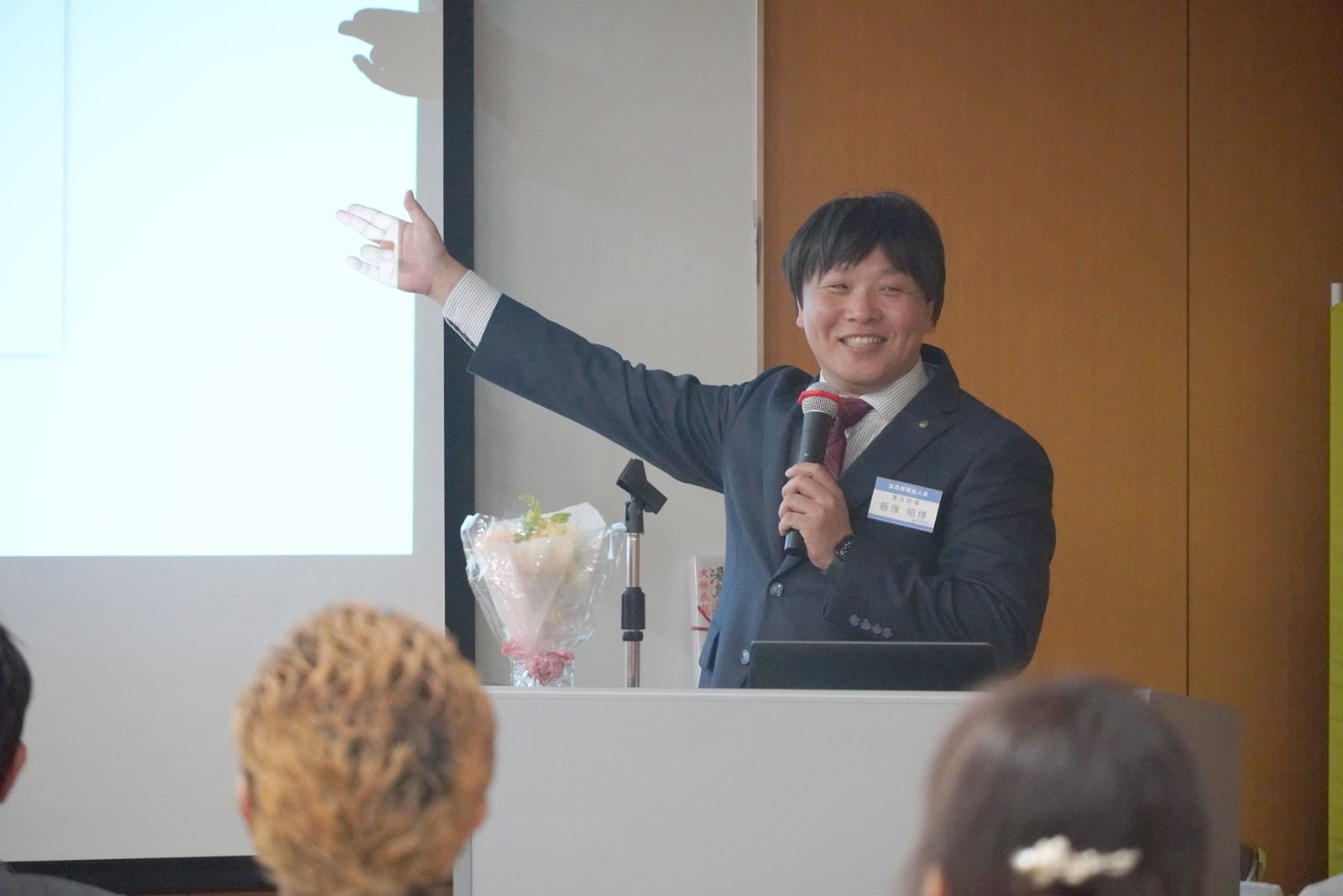 スクリーンを指し示しながら、笑顔で語り始める飯塚昭博氏