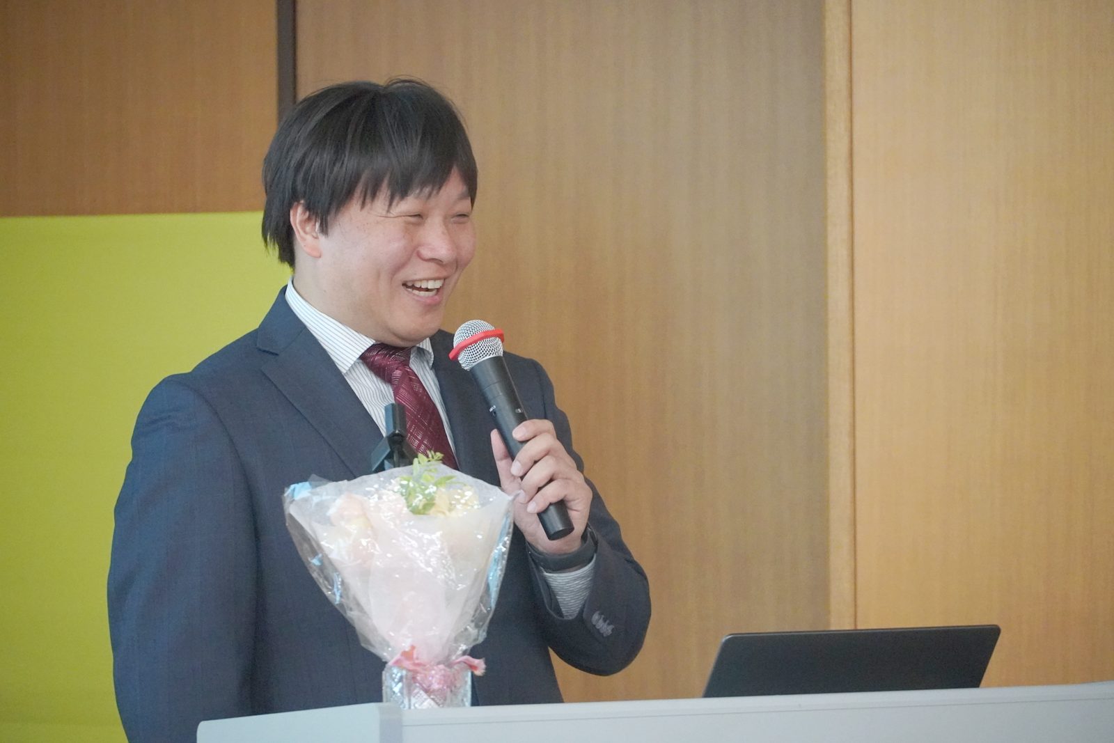 笑顔で会場に語りかける飯塚昭博氏